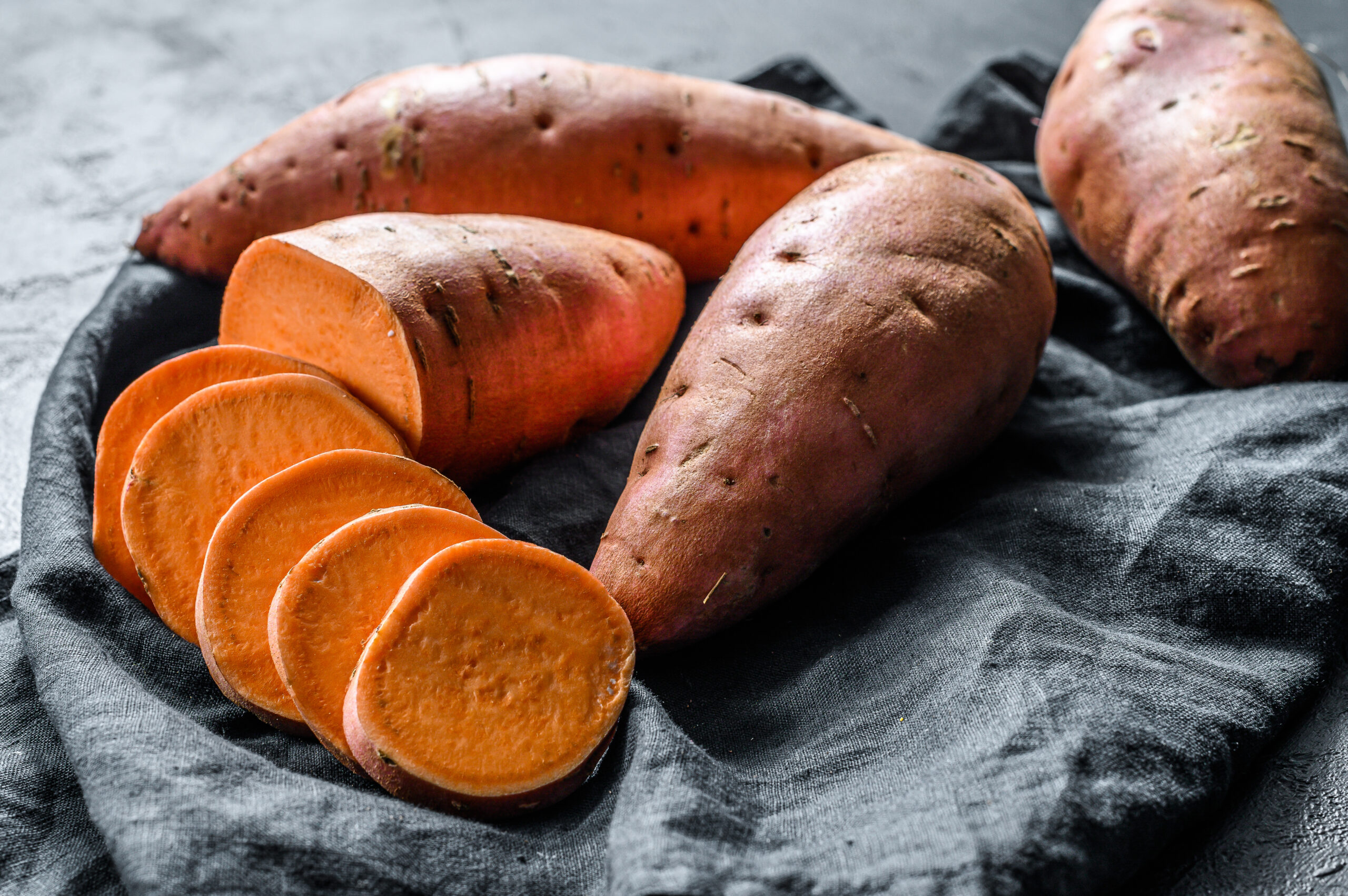 Raw sweet potatoes cut up and placed in a basket lined with a blue napkin.