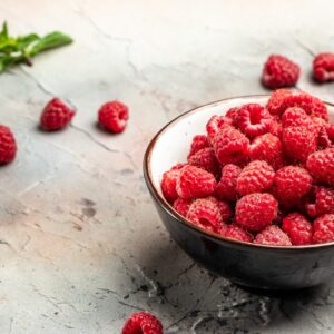 Fresh raspberries in a dark ceramic bowl on a plaster background