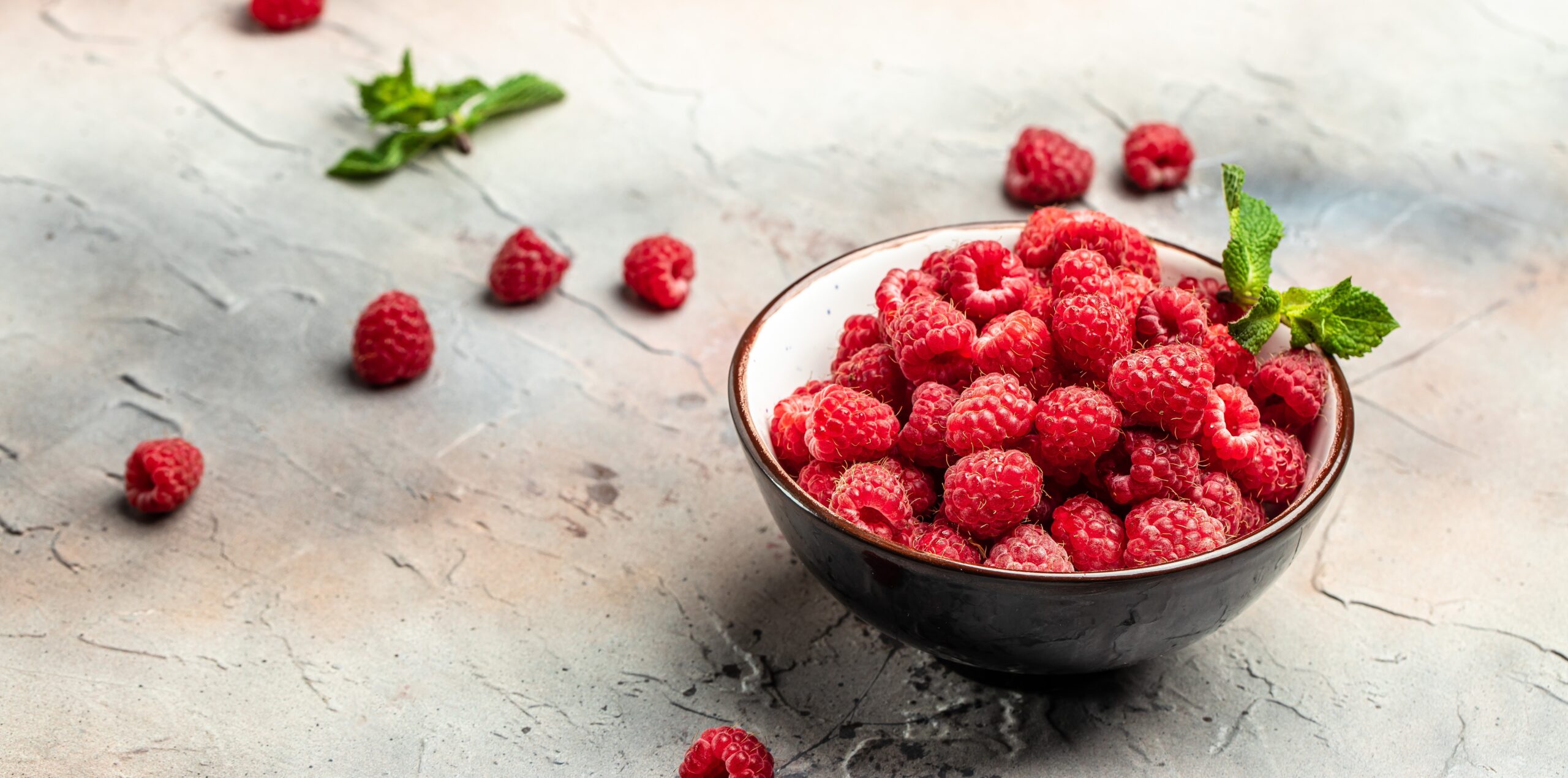 Fresh raspberries in a dark ceramic bowl on a plaster background