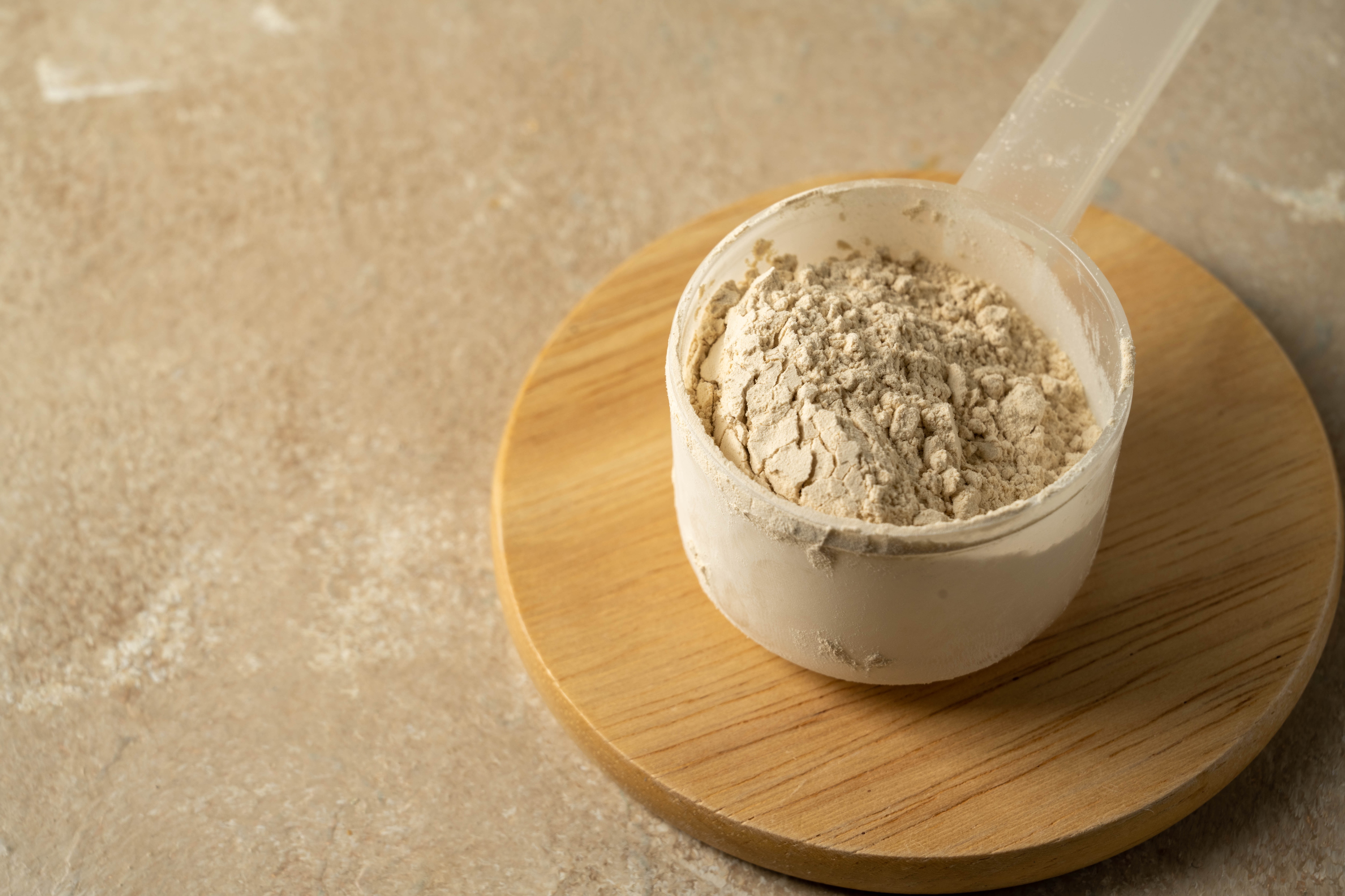 A scoop of Casein Protein powder sitting on a wooden platform on a beige background