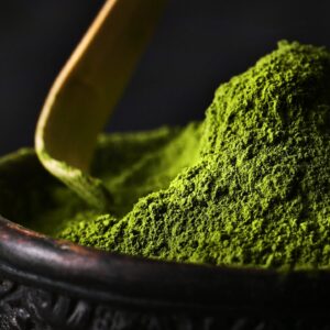 Matcha in an ornate wooden bowl being scooped by a wooden scoop.