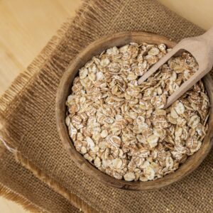 A wooden scoop sitting in a bowl of raw oats that is sitting on a woven mat.