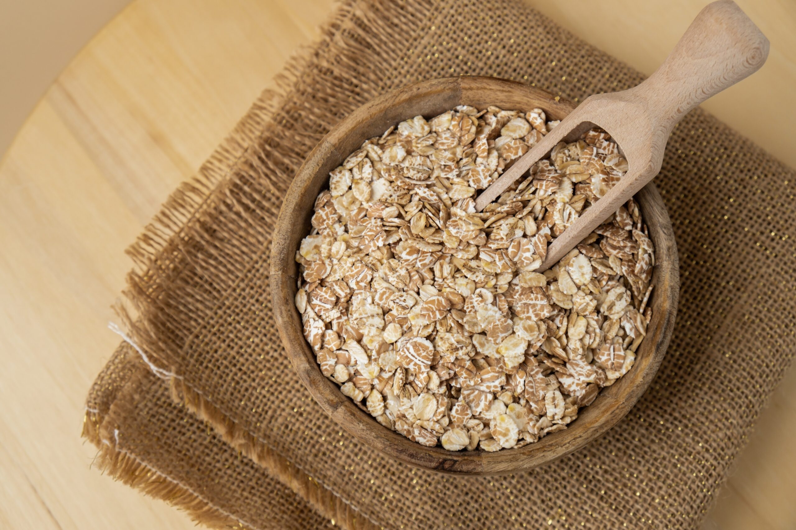 A wooden scoop sitting in a bowl of raw oats that is sitting on a woven mat.