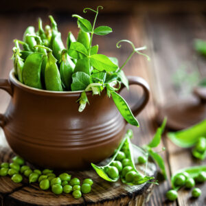 Green pea pods sitting in a decorative ceramic cup on a wooden table top